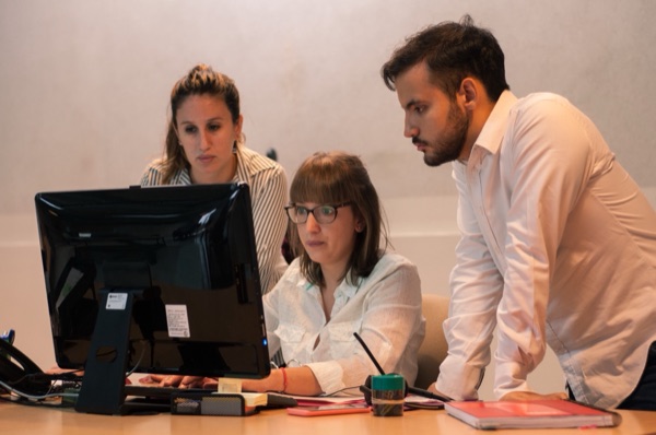 Tres colegas colaborando frente a un monitor en una oficina moderna